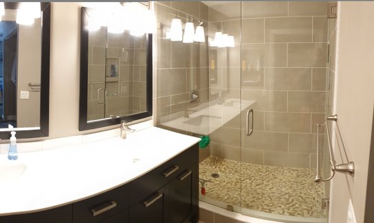 White dual sink, dark cabinet, gray wall tile and pebble floor